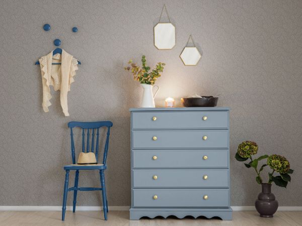 Tapeten Lycke Vår 1 på vegg med lys blå kommode foran, en mørk blå stol, knagger i mørk blå, grønne planter og noe nips oppå kommoden.