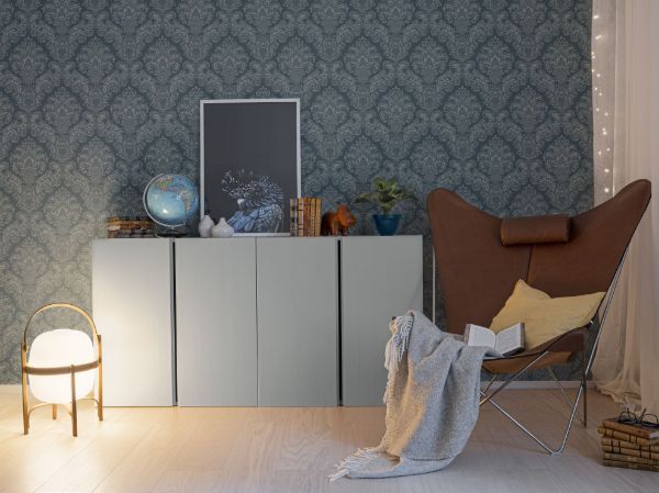 Lycke Historia 2 på vegg i en stue. Inntil veggen står et hvit skap, med dekor av bilde, globus, plante og annet nips oppå. Det står en brun skinnstol foran, med et grått teppe og gul puti oppi. En liten lampe står også på gulvet ved siden av skapet.