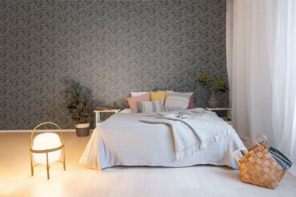Lycke Primula 2 på soveromsvegg bak en seng med hvitt sengetøy og gule og rosa puter. Det er grønnplanter på hver side av sengen, og en lampe på gulvet. En søt naturkurv er også plassert foran sengen. Det henger hvit gardiner foran vinduene ved siden av sengen.